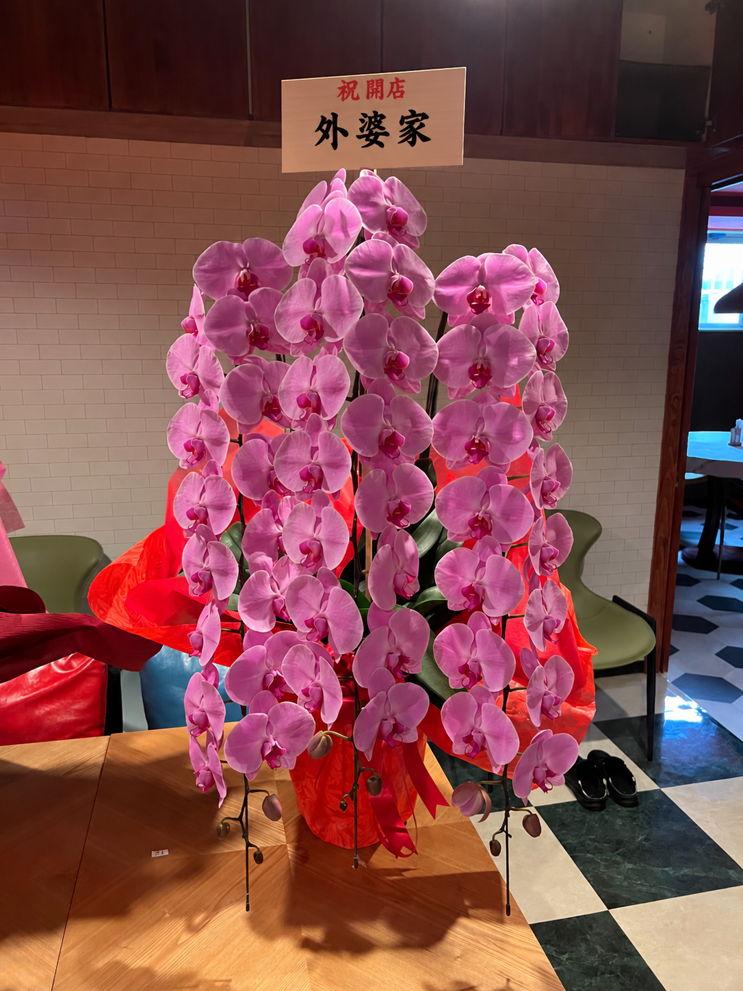 新宿三丁目の中国料理店・外婆家（ワイポージャー）様へお届けした開店祝いのピンクの胡蝶蘭。赤いラッピングと祝開店の立札